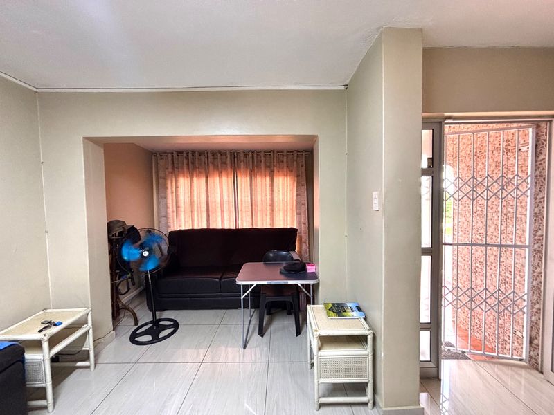 A living room area featuring tiled flooring and a recessed seating space, with direct access to an exterior security gate.