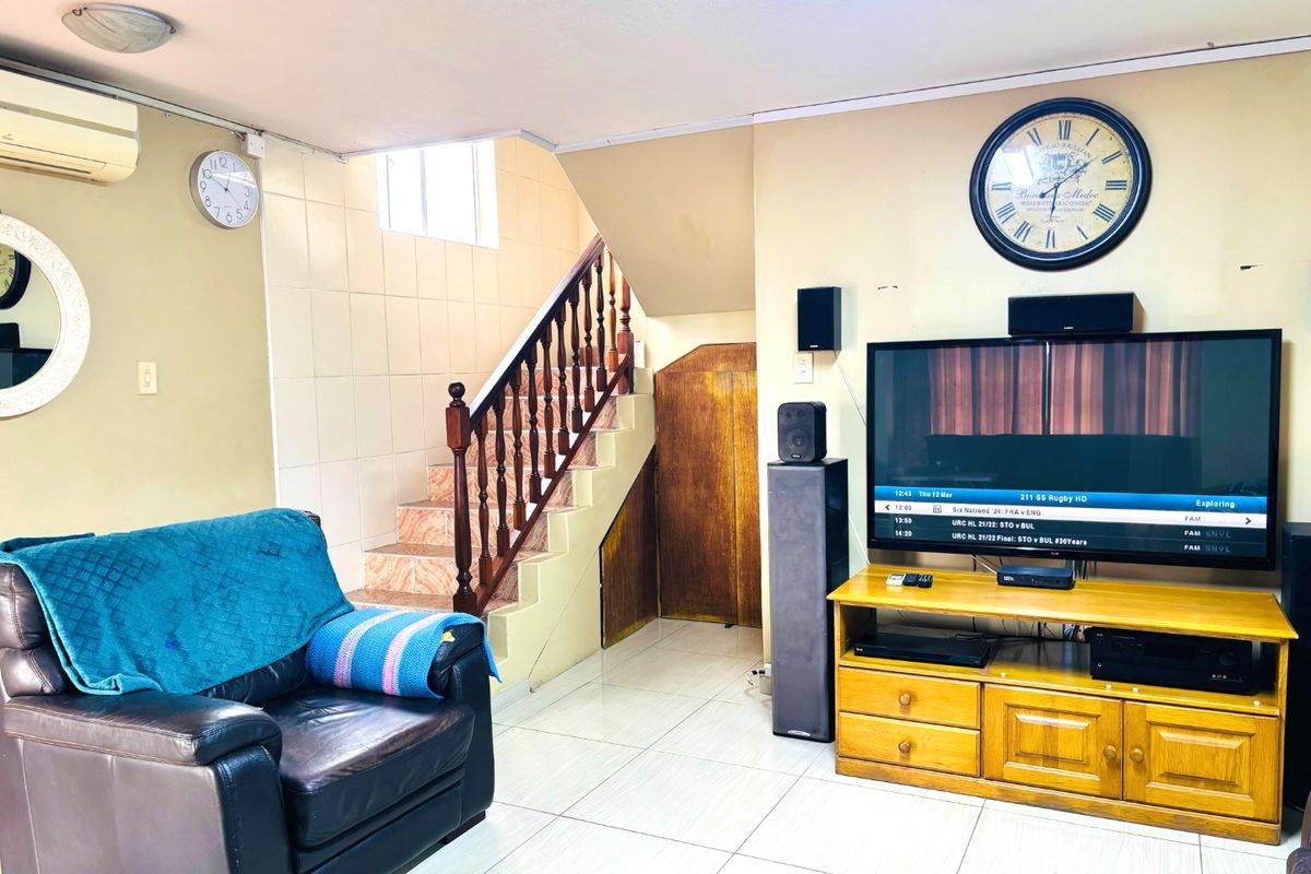 Living room featuring tiled flooring, a staircase with a wooden balustrade, built-in under-stair storage, and a wall-mounted air conditioning unit.