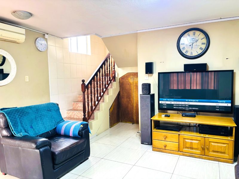 Living room featuring tiled flooring, a staircase with a wooden balustrade, built-in under-stair storage, and a wall-mounted air conditioning unit.
