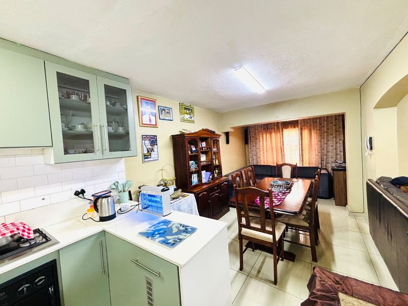 Open-plan kitchen and dining area featuring light green cabinetry, subway tile backsplash, and tiled flooring, creating a functional living space.