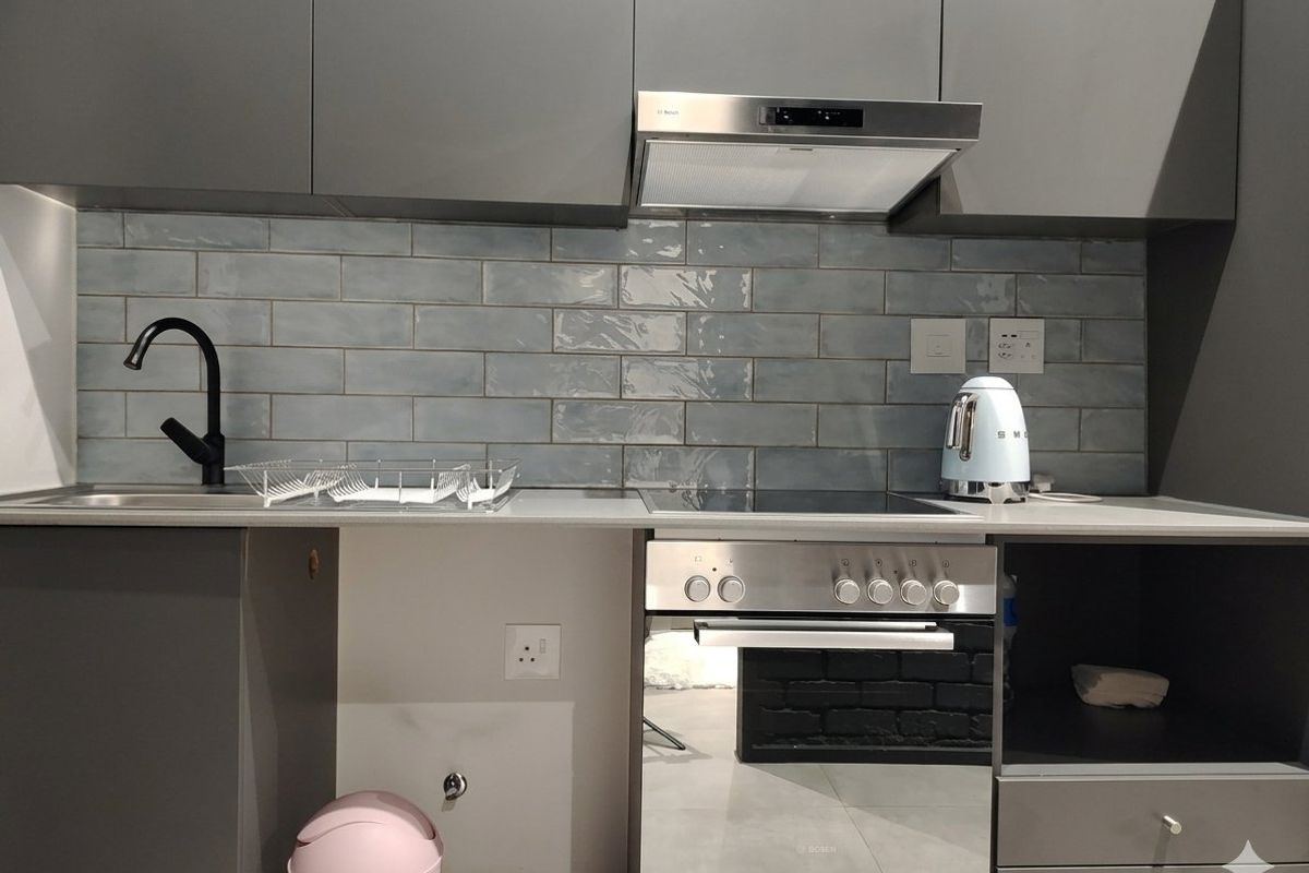 Modern kitchen featuring grey cabinetry, a blue subway tile backsplash, integrated stainless steel oven, electric cooktop, and a sleek black mixer tap.