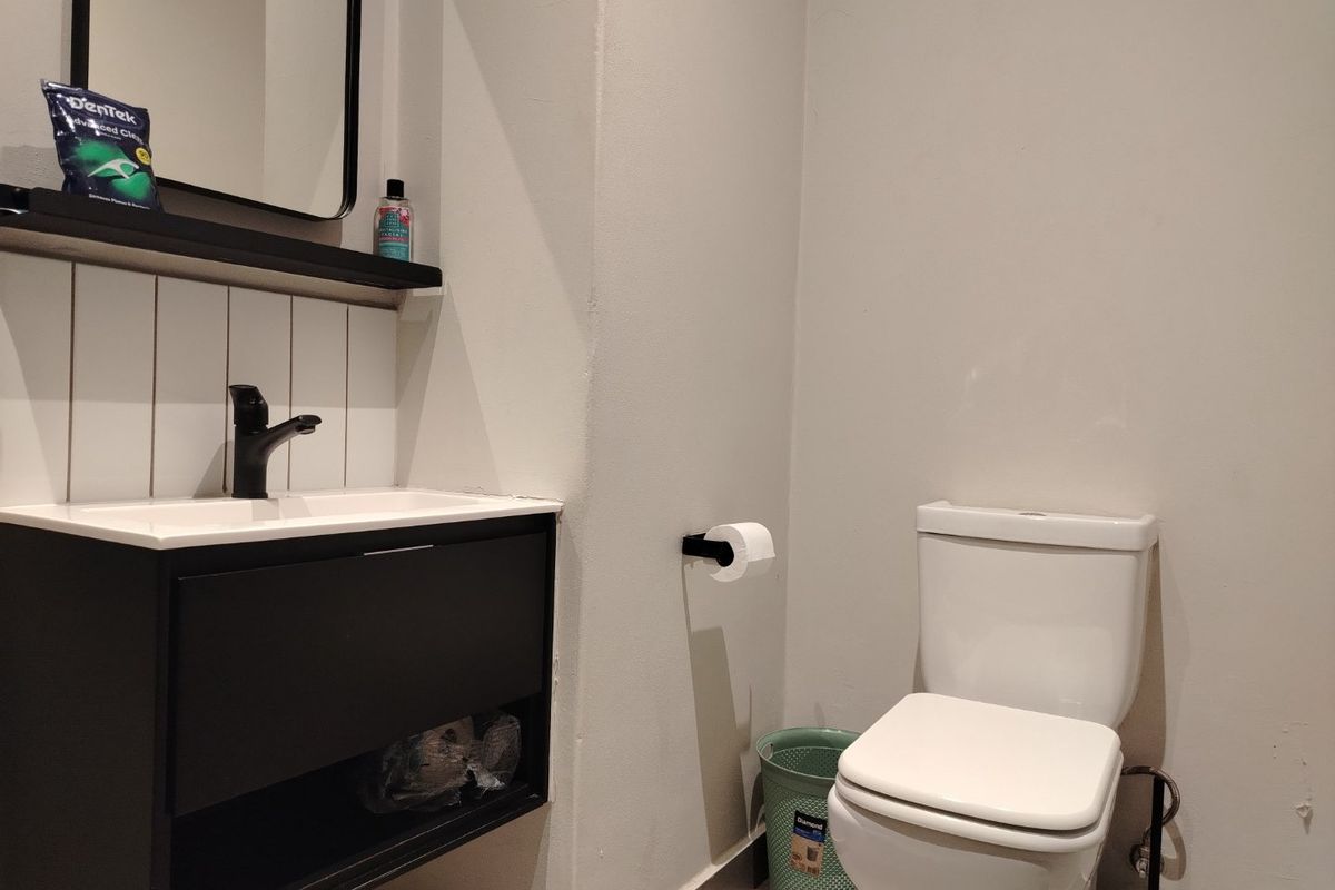 A modern bathroom featuring a wall-mounted vanity with a black mixer tap, a white toilet, and a tiled splashback with a matching mirror.