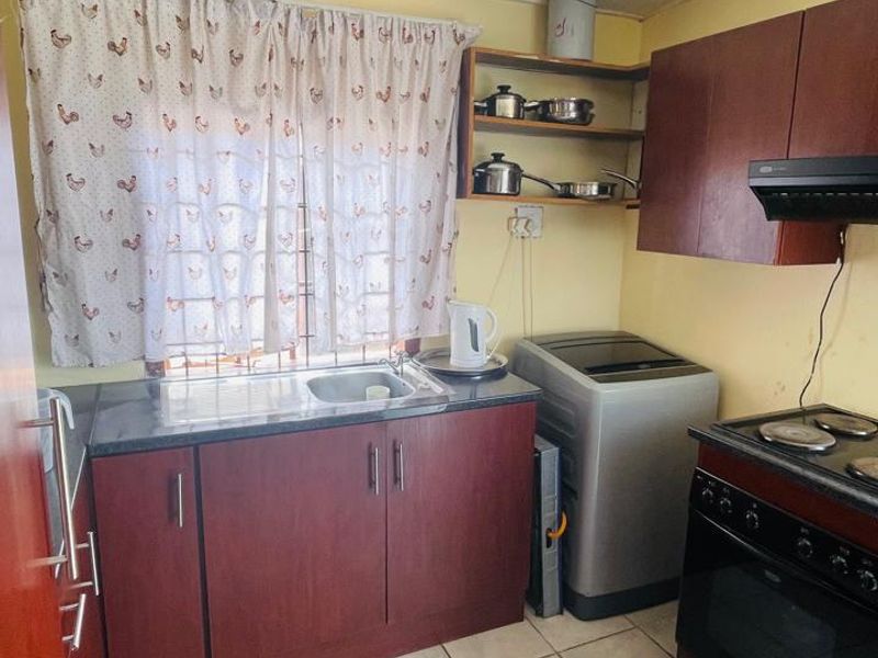 Compact kitchen featuring dark wood cabinetry, granite countertops, built-in oven with hob, and tiled flooring, offering a functional layout with potential for modernization.
