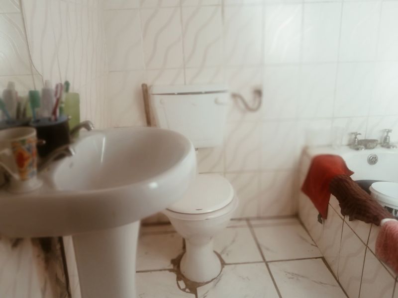 A dated bathroom featuring a pedestal basin, toilet, and bathtub with white tiled walls and flooring, requiring cosmetic updates.