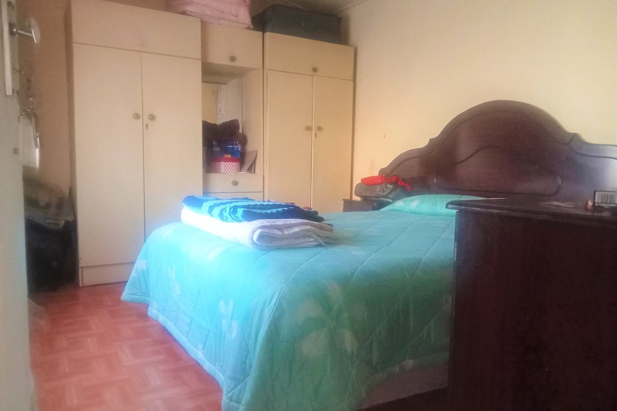 A bedroom featuring built-in cupboards and tiled flooring, offering a functional space with potential for cosmetic updates.