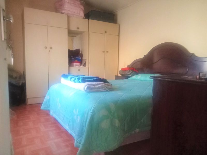 A bedroom featuring built-in cupboards and tiled flooring, offering a functional space with potential for cosmetic updates.