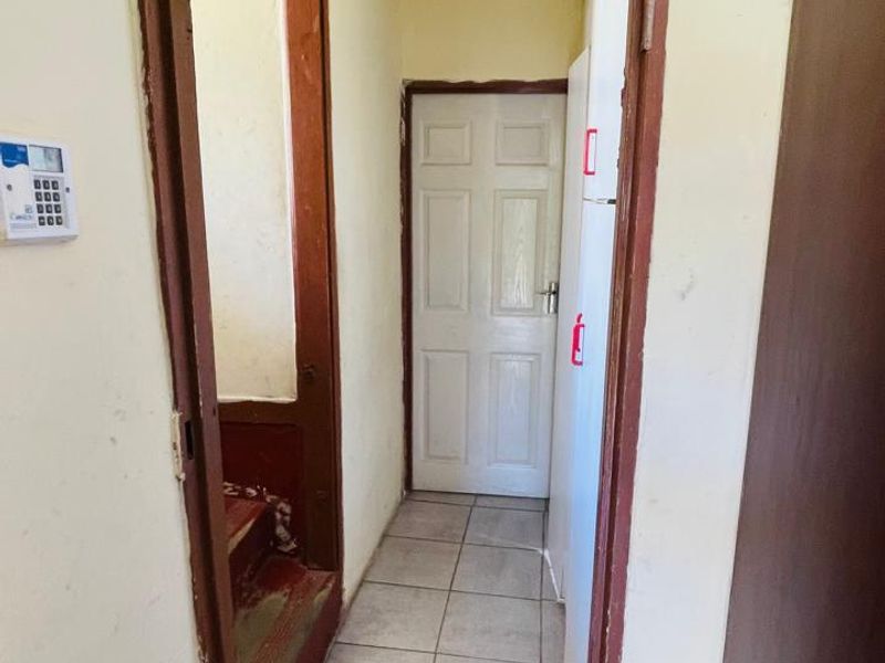 A functional hallway featuring tiled flooring, timber door frames, and a wall-mounted security alarm keypad.