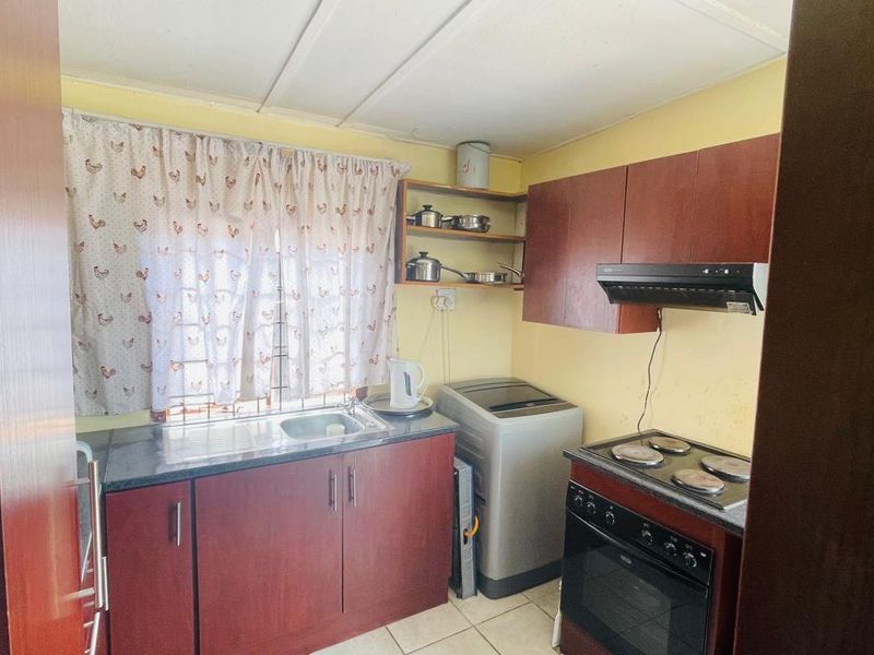 A compact kitchen featuring dark wood-look cabinetry, laminate countertops, a stainless steel sink, and a freestanding stove with an extractor fan.