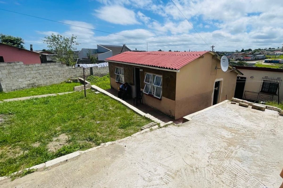 Rear view of a detached house featuring a corrugated metal roof, concrete patio area, and a surrounding boundary wall.
