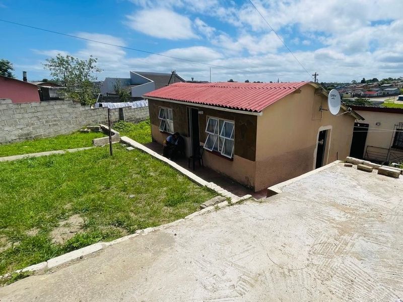 Rear view of a detached house featuring a corrugated metal roof, concrete patio area, and a surrounding boundary wall.