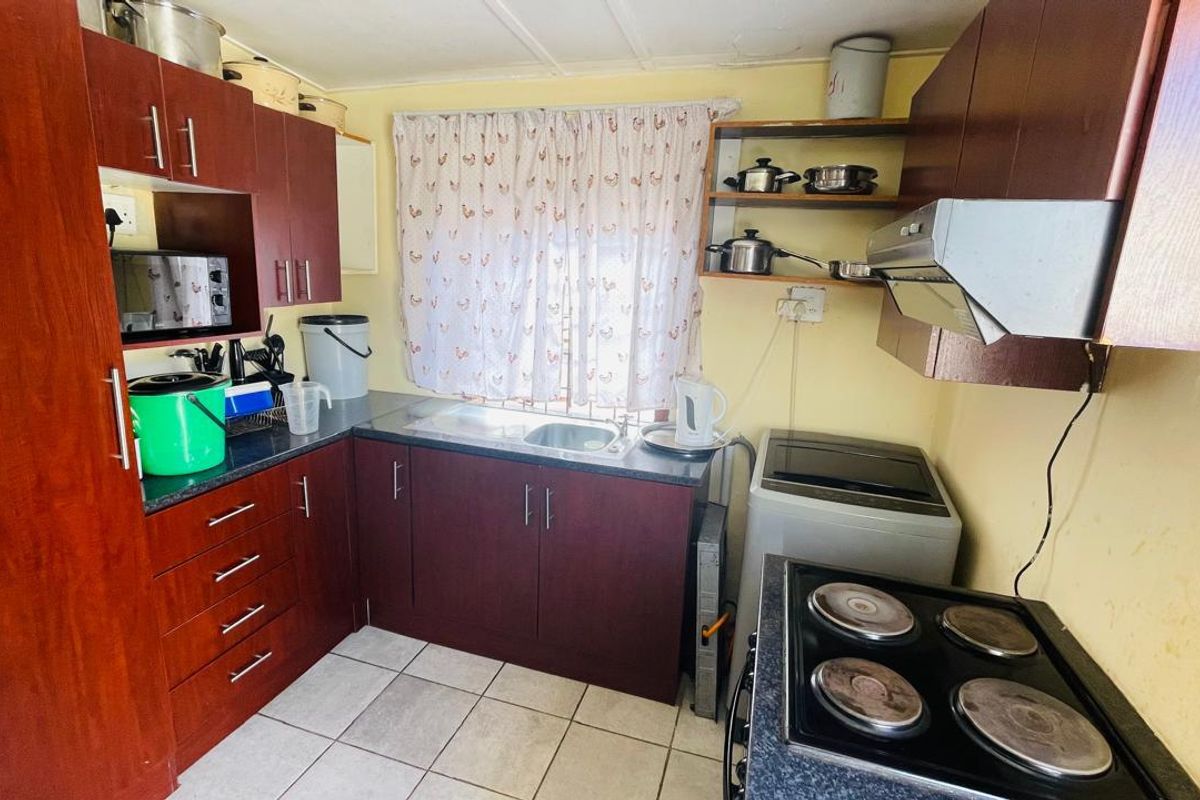 A compact kitchen featuring dark laminate cabinetry, a stainless steel sink, an electric stove with an extractor fan, and tiled flooring.