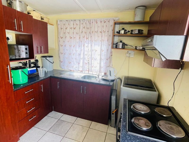 A compact kitchen featuring dark laminate cabinetry, a stainless steel sink, an electric stove with an extractor fan, and tiled flooring.