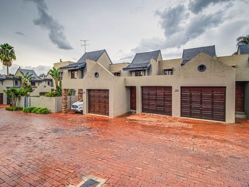 Front exterior view of a residential complex featuring multiple garage doors, brick paved driveway, and a well-maintained stucco facade under a cloudy sky.