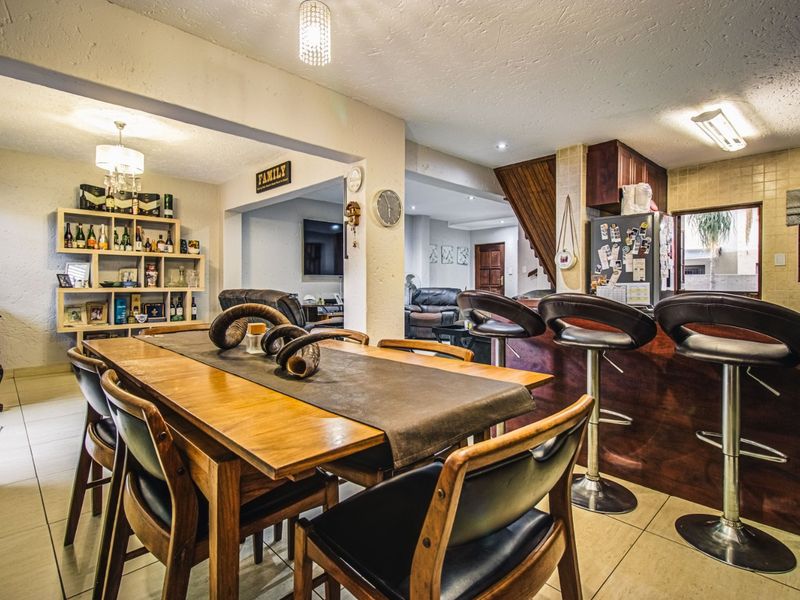 Open-plan living and dining area featuring tiled flooring, a breakfast bar with built-in cabinetry, and integrated lighting throughout the connected space.