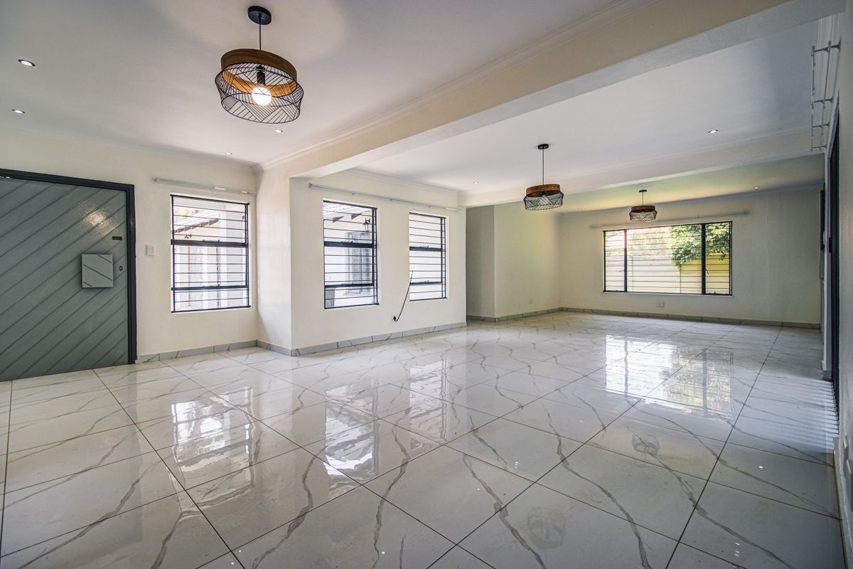 Spacious, open-plan living area featuring polished marble-look porcelain tiles, modern pendant lighting, and large windows with security bars.