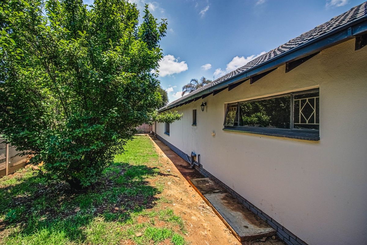 A view of the rear exterior of the house featuring a tiled roof, security-barred windows, and a concrete pathway along the foundation.