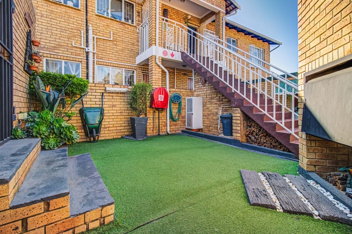 A rear courtyard area featuring a brick facade, artificial turf, and an external staircase with metal railings leading to the upper level.