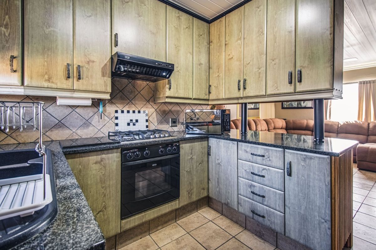 A functional kitchen featuring wooden cabinetry, granite countertops, a gas hob, built-in oven, and tiled finishes, offering a practical layout for daily cooking.