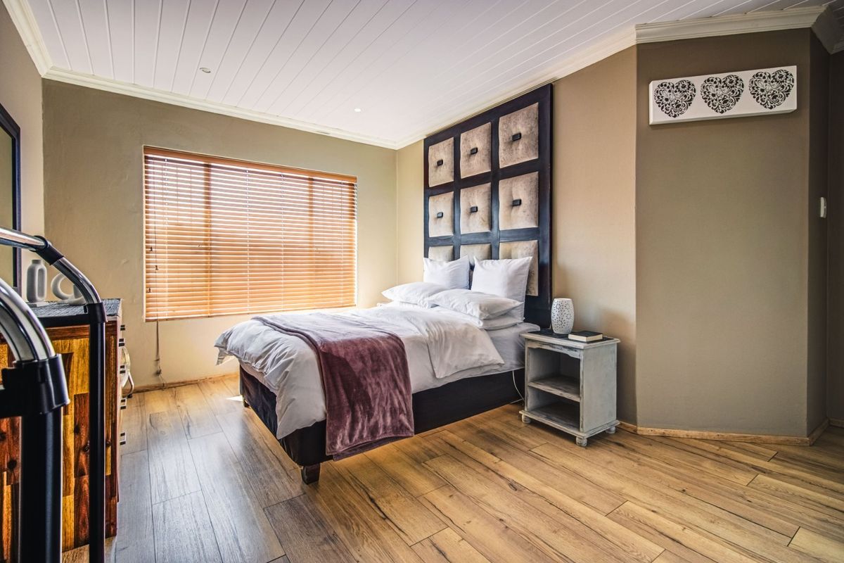 A bedroom featuring wood-look laminate flooring, a tongue and groove ceiling, and a custom built-in headboard with venetian blinds.
