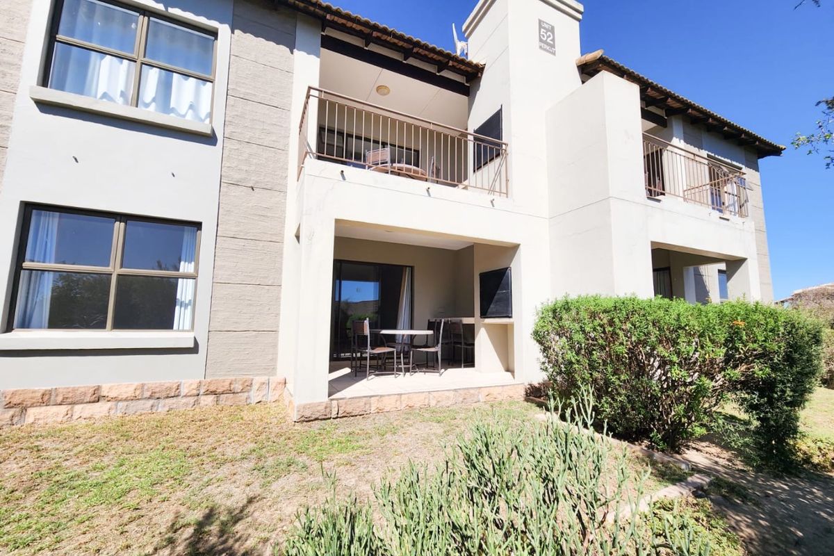 Exterior view of an apartment building featuring a ground-floor patio with a built-in braai and an upper-level balcony with metal railings.