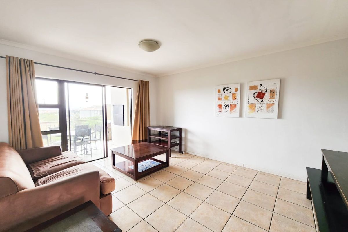 A bright living room featuring neutral ceramic floor tiles and large sliding glass doors that provide access to an outdoor balcony area.