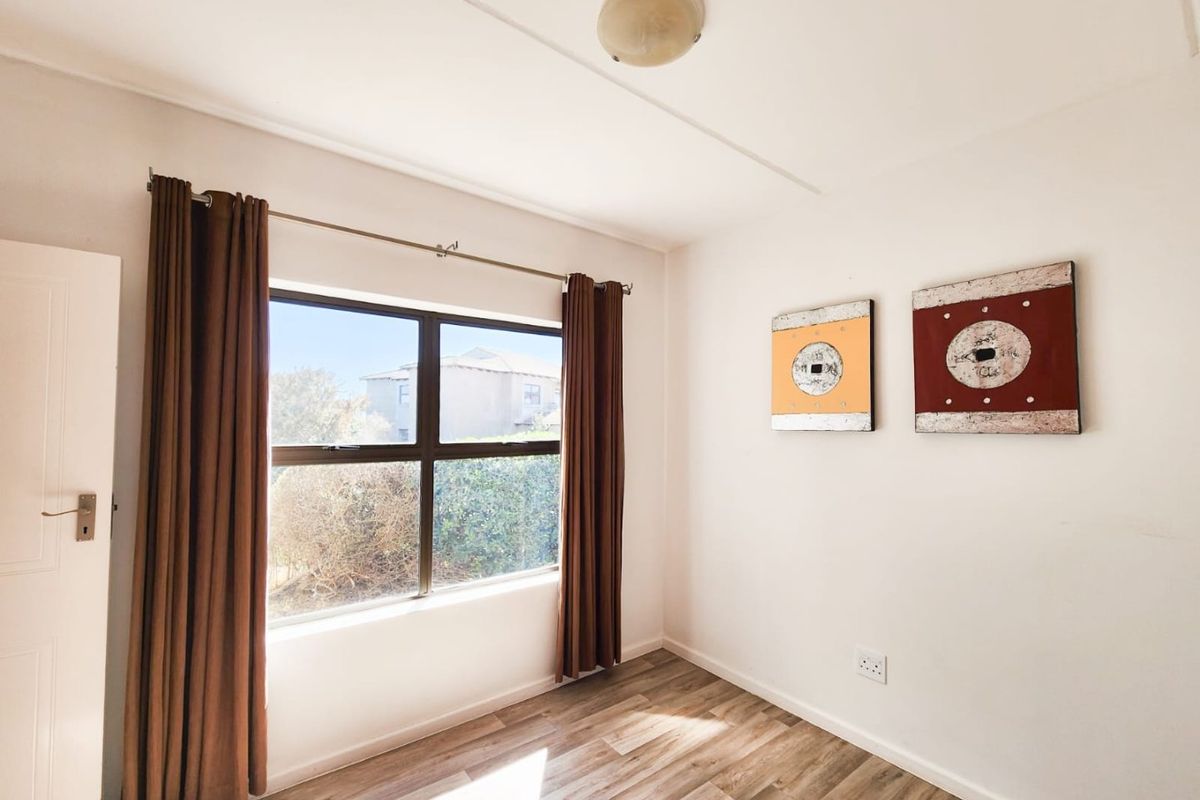 A bright, empty bedroom featuring wood-look laminate flooring, a large window with curtain rod, and a central ceiling light fixture.