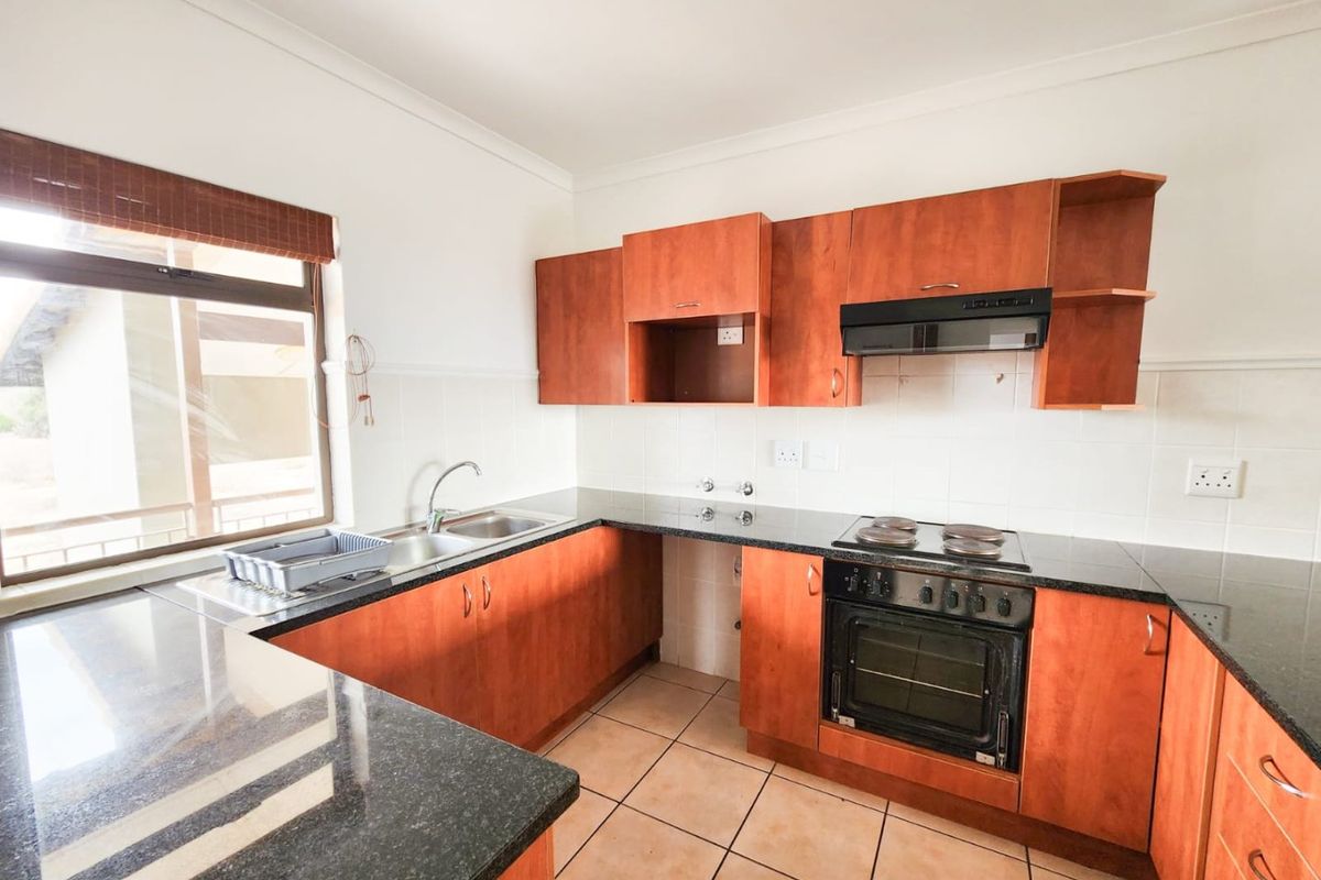 Functional kitchen featuring dark granite countertops, wooden cabinetry, built-in oven, electric hob, and extractor fan with tiled flooring.