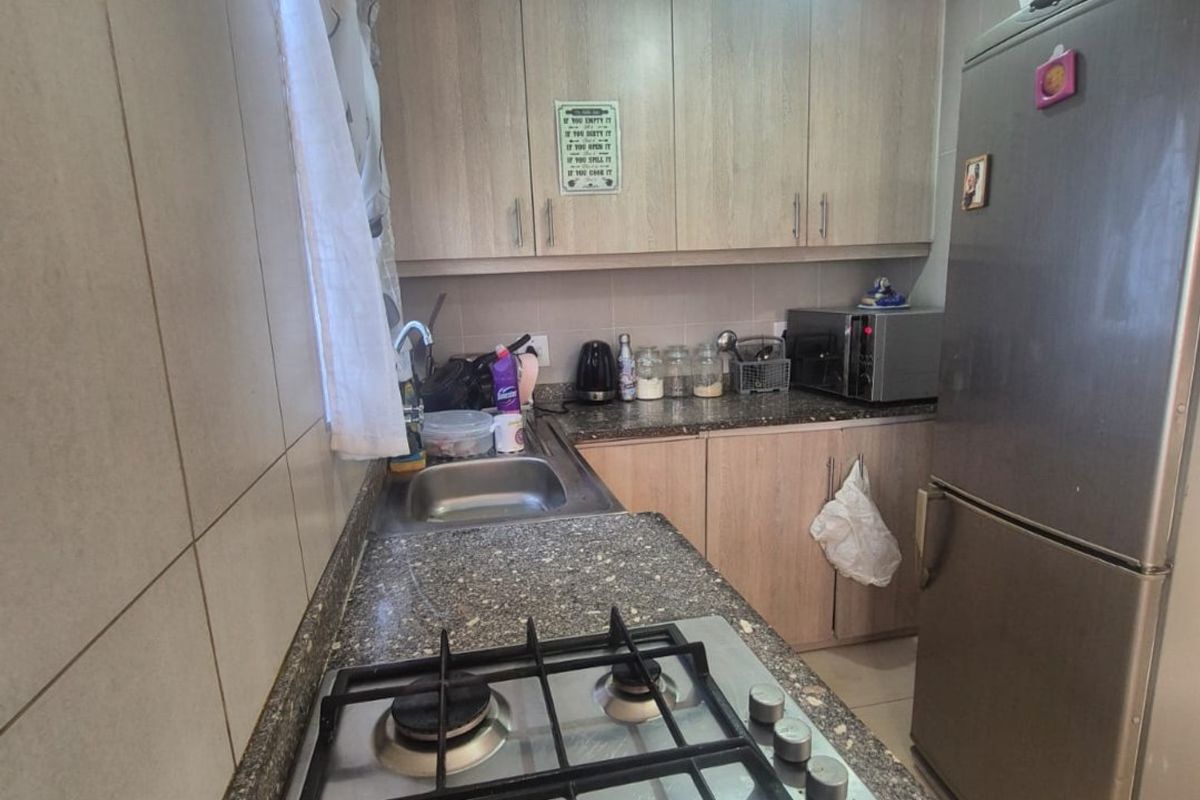A functional kitchen featuring light wood-finish cabinetry, granite countertops, a gas hob, and tiled splashbacks with decorative coving.