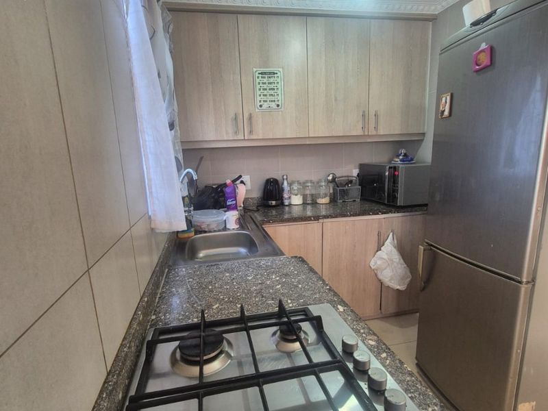 A functional kitchen featuring light wood-finish cabinetry, granite countertops, a gas hob, and tiled splashbacks with decorative coving.