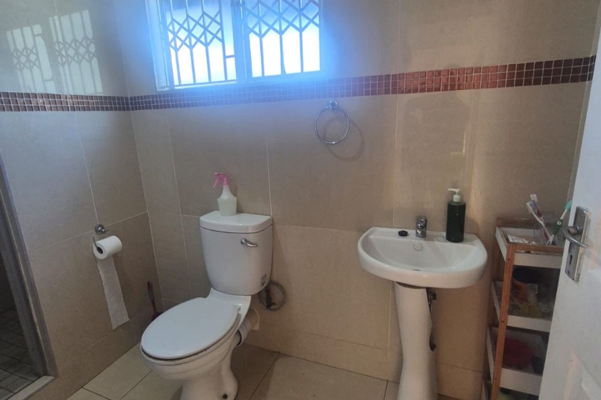 A functional bathroom featuring a pedestal basin, toilet, and shower enclosure with neutral wall and floor tiling.