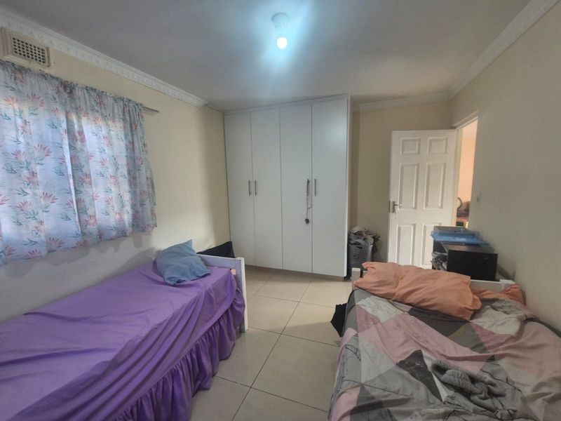A functional bedroom featuring tiled flooring, built-in cupboards, and decorative ceiling cornicing.