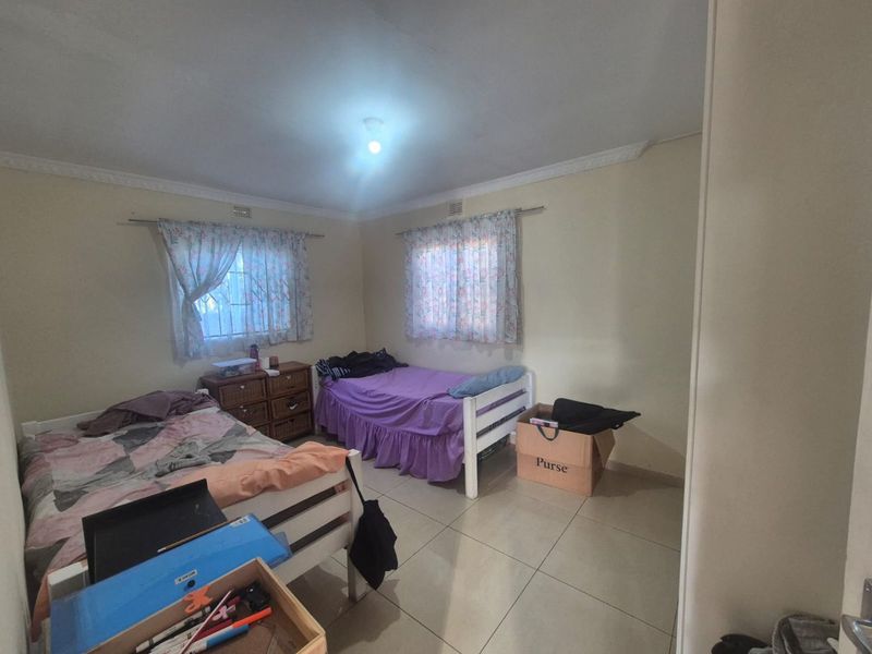 A functional bedroom featuring tiled flooring, decorative cornicing, and windows fitted with security bars.