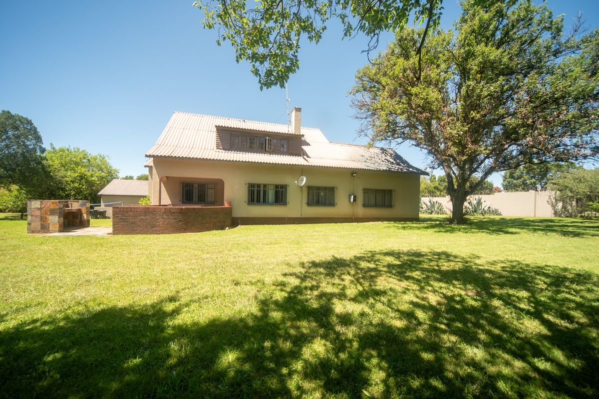 Rear view of the house featuring a spacious lawn, a built-in brick braai area, and a tiled roof structure.