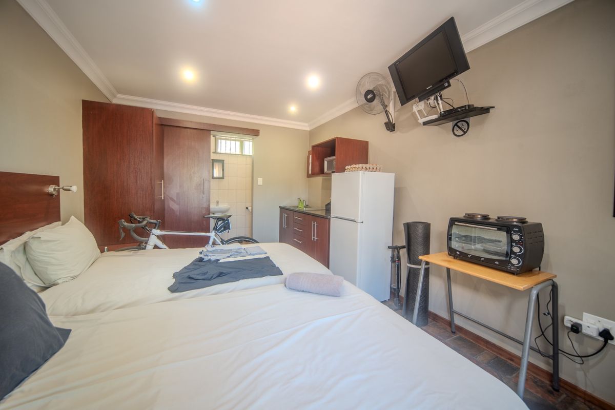 A bedroom featuring built-in cupboards, recessed downlighting, and tiled flooring, with an integrated kitchenette area and access to an en-suite bathroom.
