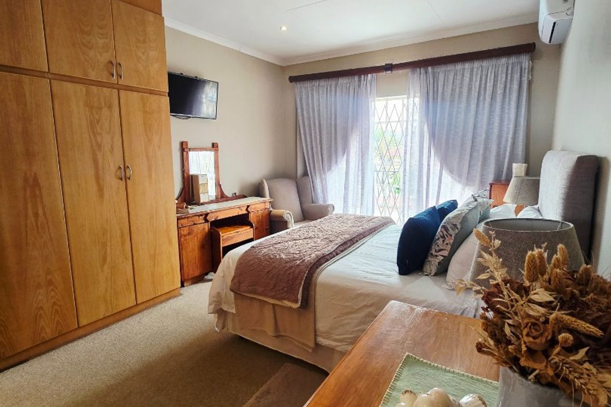 A well-proportioned bedroom featuring built-in wooden cupboards, carpeted flooring, and an air conditioning unit, with direct access to a balcony through a security gate.