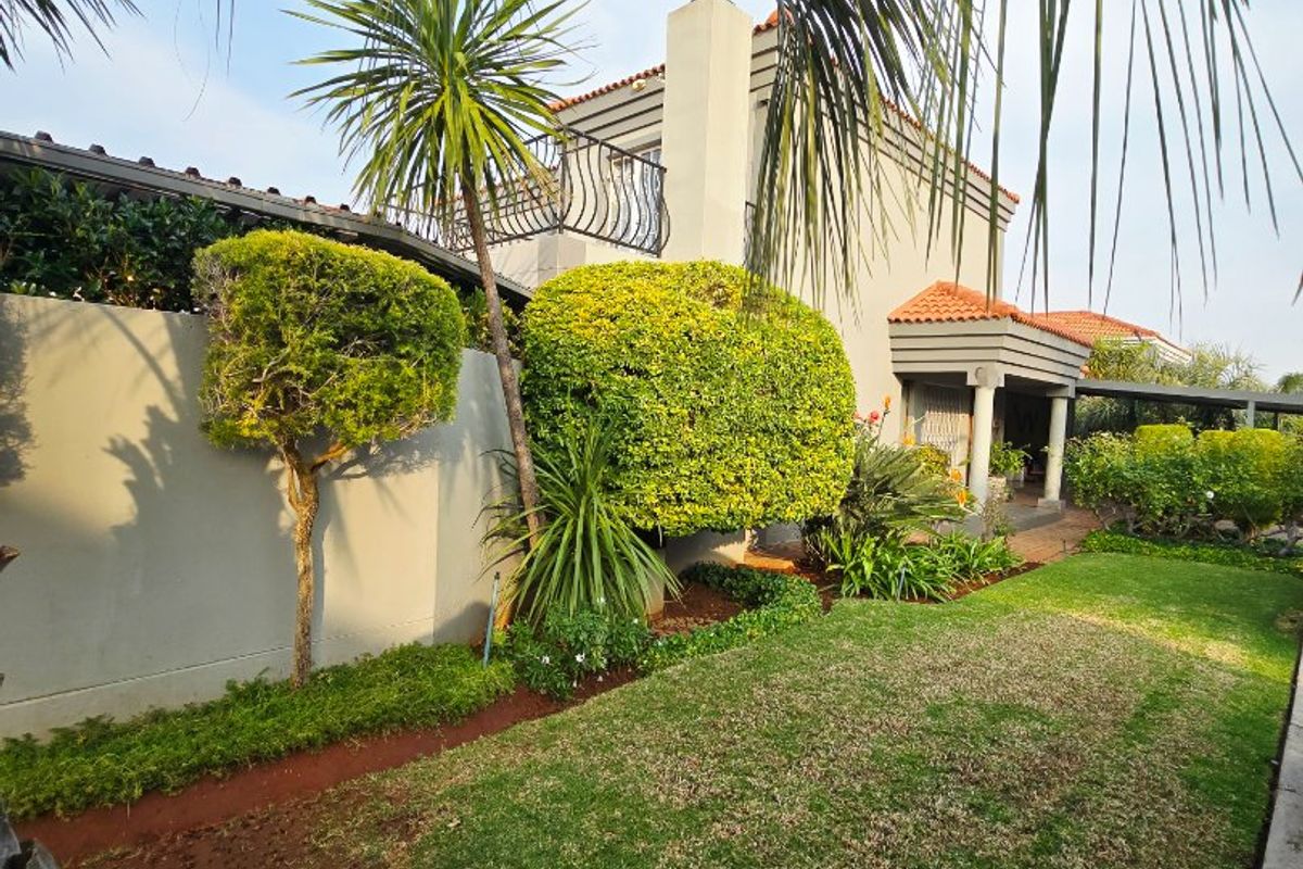A well-maintained rear garden featuring a manicured lawn, established landscaping, and a view of the home's exterior with a balcony and covered patio area.