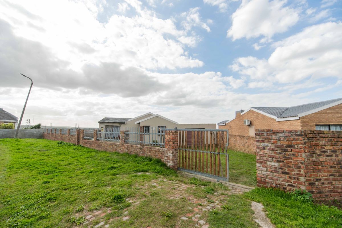 A view of the rear exterior of the property featuring a brick boundary wall, metal security fencing, and a gated entrance to the yard.