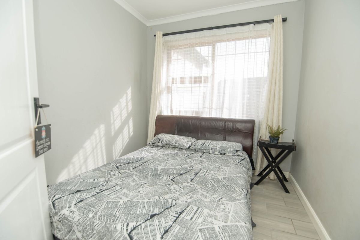 A compact bedroom featuring light-toned tiled flooring, neutral wall finishes, and a window with natural light exposure.
