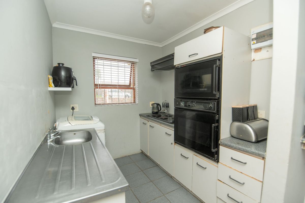 Compact kitchen featuring built-in oven, microwave, hob, extractor fan, stainless steel sink, and tiled flooring with ample storage cabinetry.