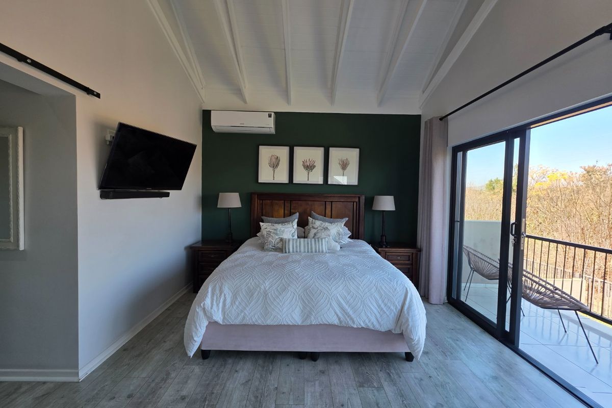 A well-maintained bedroom featuring exposed beam ceilings, split-system air conditioning, and sliding glass doors leading to a private balcony.