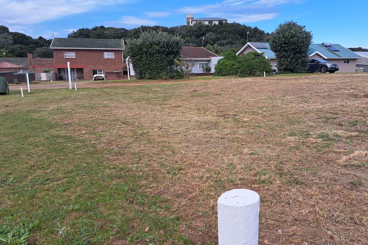 A vacant residential plot of land featuring grass coverage and visible boundary markers, situated in a developed neighborhood setting.