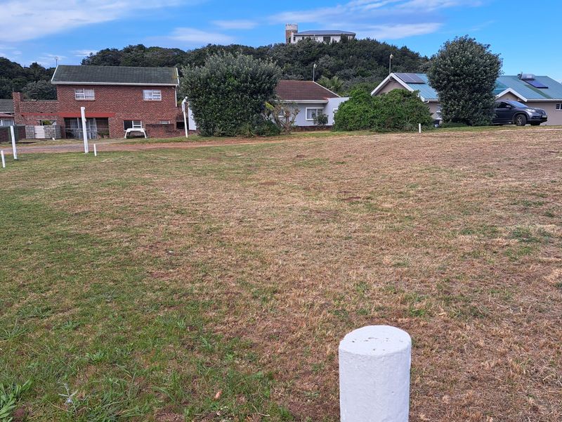 A vacant residential plot of land featuring grass coverage and visible boundary markers, situated in a developed neighborhood setting.
