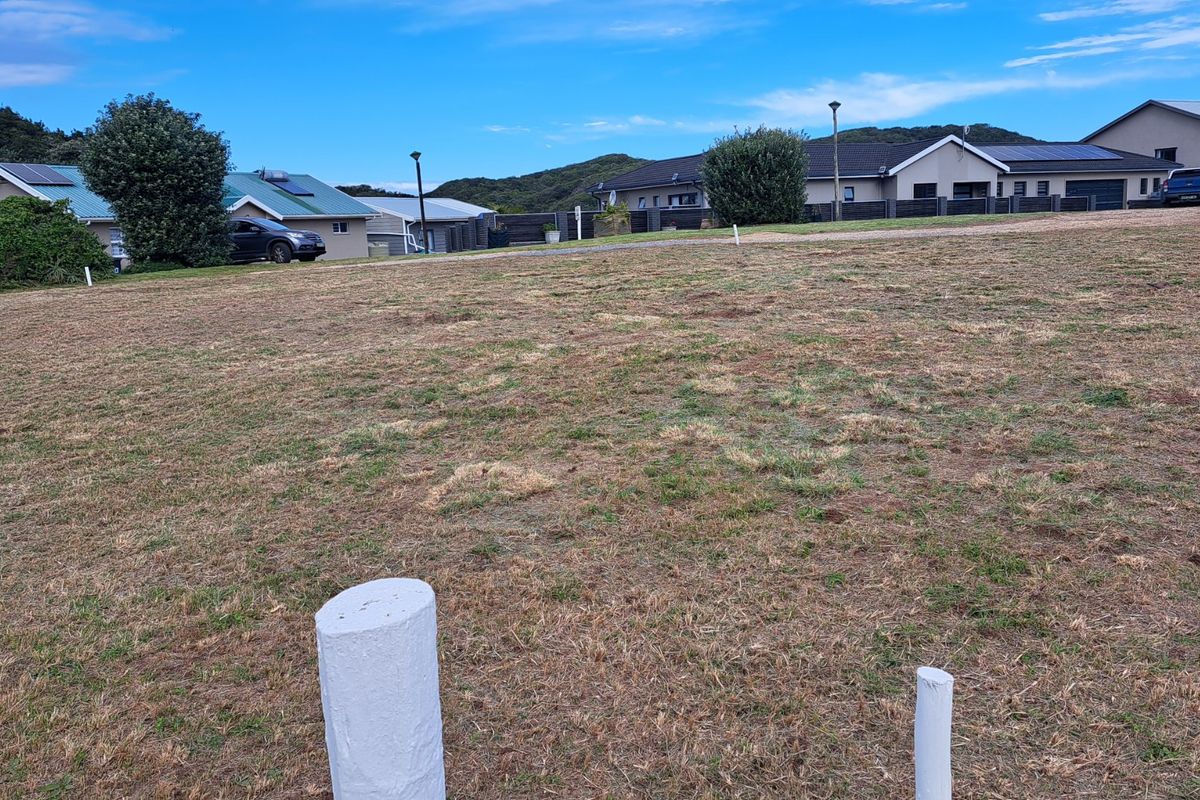 A vacant residential plot of land featuring established grass and visible survey markers, situated within a developed neighborhood setting.