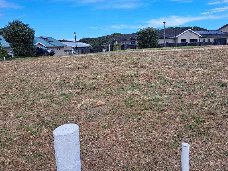 A vacant residential plot of land featuring established grass and visible survey markers, situated within a developed neighborhood setting.