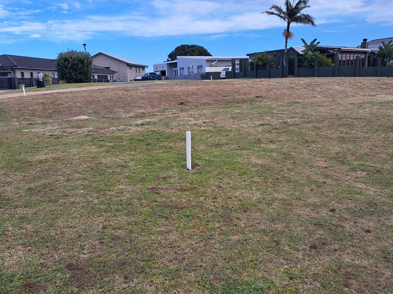 A vacant residential plot of land featuring grass coverage and visible survey pegs, situated in a developed neighborhood.