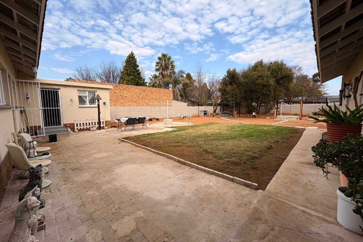 Spacious rear garden featuring a paved patio area, central lawn, and secure boundary walls, offering a functional outdoor space for the property.