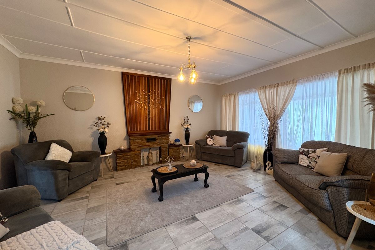 A spacious living room featuring a stone fireplace, tiled flooring, and decorative ceiling panels, offering a comfortable and well-maintained living space.