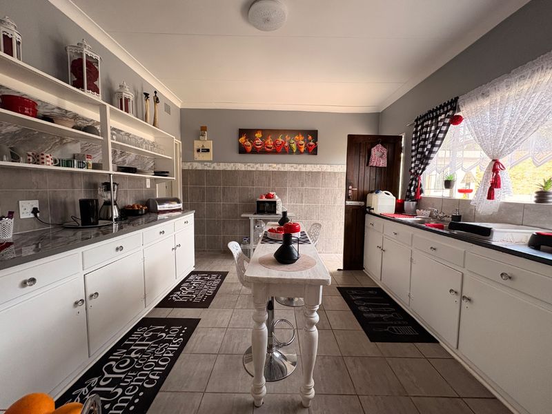 A functional kitchen featuring white cabinetry, tiled backsplash, open shelving, and a central breakfast bar area with tiled flooring throughout.
