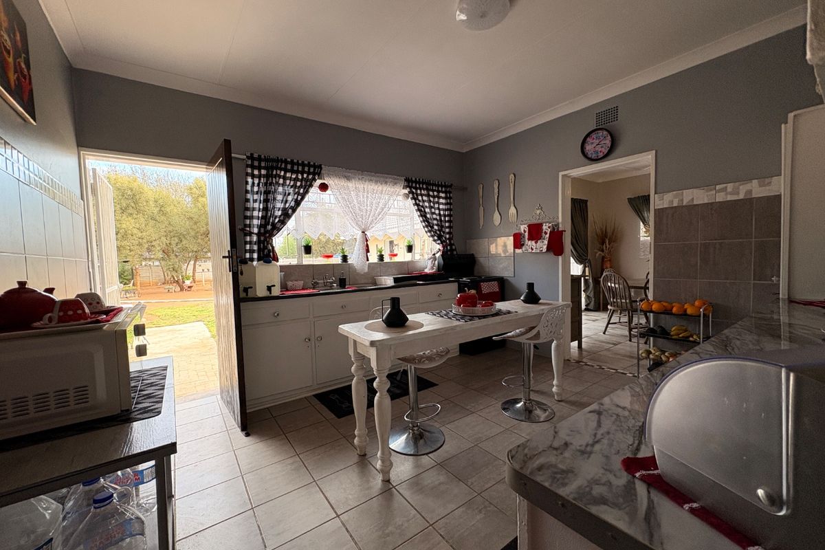 A functional kitchen featuring tiled flooring, built-in cabinetry, and a tiled backsplash, with direct access to the rear garden area.