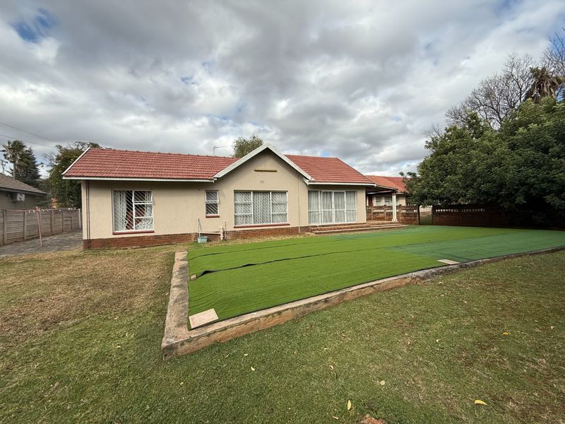 Rear view of the house featuring a tiled roof, sliding glass doors, and a raised artificial lawn area in the backyard.